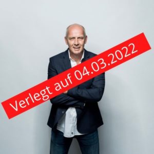 Bario Basler vor grau weisem Hintergrund verschränkt die Arme und schaut in die Kamera. Darüber ein roter Balken mit dem Schriftzug Verlegt auf 04.03.2022