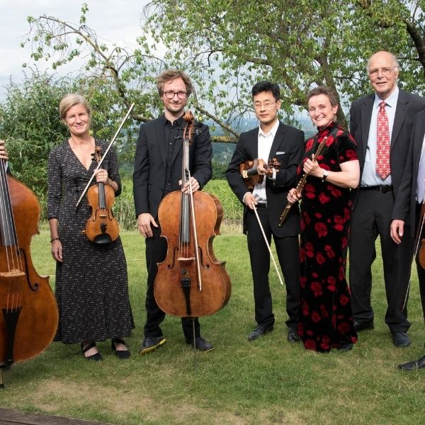 Ein Ensemble des Mainzer Kammerorchesters steht mit Instrumenten auf einer grünen Wiese
