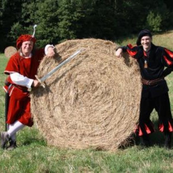 Die beiden Schauspieler vom Rittermahl in Kostümen auf einer Wiese neben einem Heuballen