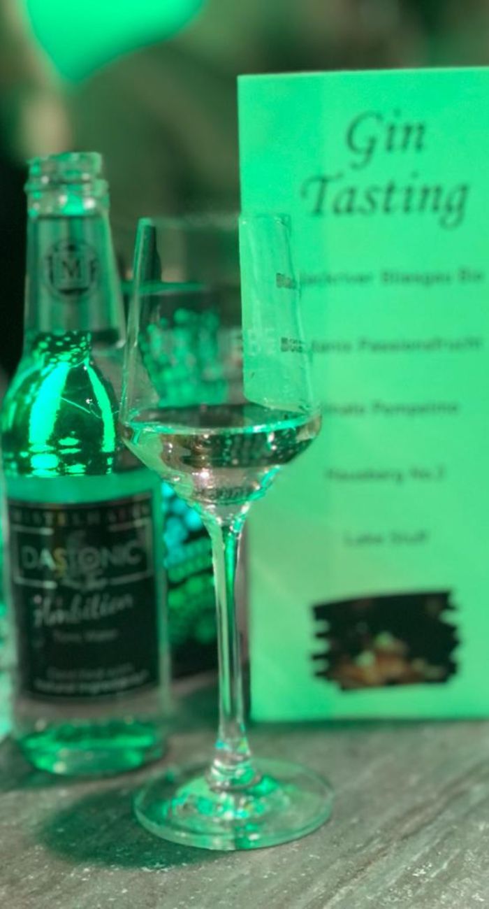 Ein Gin Nosing Glas, sowie eine Flasche Tonic Water und ein Tischaufsteller in grünem Licht