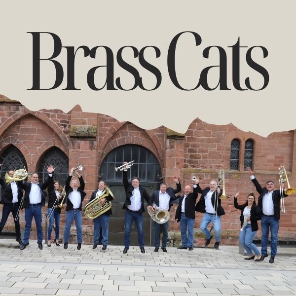 Die Band BrassCats steht vor einer Kirche mit ihren Instrumenten und springt dabei in die Luft