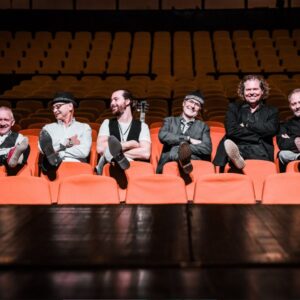 Marcel Adam und Band sitzen vor einer bühne auf Roten Sitzplätzen